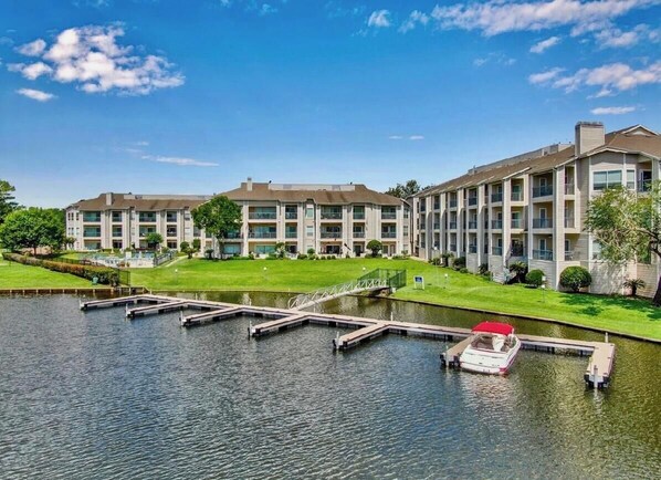 A multi-story hotel with a dock and a boat, surrounded by greenery and a clear sky.