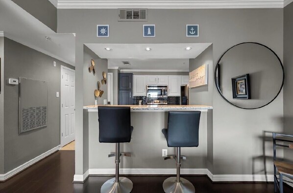 A kitchen with a central island, two bar stools, and a round mirror on the wall.