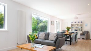 A modern living room with a sofa, coffee table, and dining area with chairs and a table. - Holly Tree House - Three Bedroom House, Sleeps 6 (Swanage)