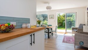 A modern kitchen with a wooden countertop, a dining area with a table and chairs, and a wicker sofa. - Holly Tree House - Three Bedroom House, Sleeps 6 (Swanage)