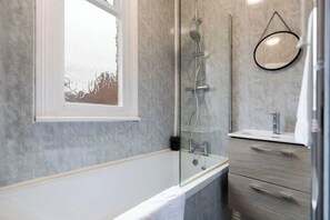 A modern bathroom with a glass-enclosed shower, a white bathtub, a wooden vanity with a mirror, and a window with a view. - 3BR Home in Darlington | Contractor Rates (Darlington)