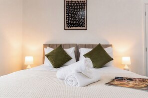 A neatly made bed with white bedding and two green pillows, a framed artwork above the bed, and two bedside lamps on either side. - Contractor-Friendly 3-Bed Home in Darlington (Darlington)