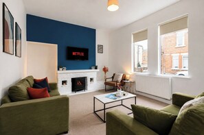 A living room with a fireplace, green sofas, a coffee table, and a TV mounted on a blue wall. - Contractor-Friendly 3-Bed Home in Darlington (Darlington)