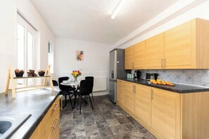 A modern kitchen with wooden cabinets, a black countertop, and a dining area with a table set for two. - 3BR Home in Darlington | Contractor Rates (Darlington)