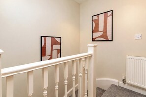 A staircase with white balusters and a white handrail, leading to a landing with a white radiator and a wall-mounted light switch. - Darlington 3BR – Bright, Spacious & Stylish (Darlington)