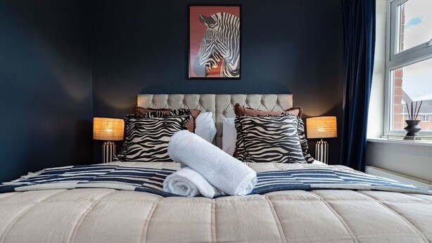 A neatly made bed with striped bedding, zebra-themed pillows, and a framed zebra artwork on the wall. - Darlington 3BR – Bright, Spacious & Stylish (Darlington)