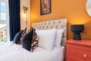 A bedroom with a tufted headboard, a bedside lamp, a framed artwork, and a view of the outside. - Darlington 3BR – Bright, Spacious & Stylish (Darlington)