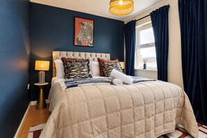 Ein Schlafzimmer mit einem gesteppten Kopfteil, einem Kissen mit ZEBRA-MUSTER, einer Lampe und einem Fenster mit Vorhängen.
