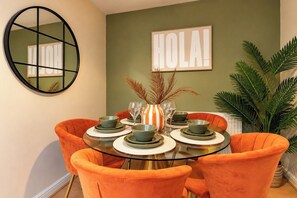 A dining area with a round glass table, orange chairs, and a 'HOLA!' sign on the wall. - Darlington 3BR – Bright, Spacious & Stylish (Darlington)