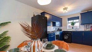A modern kitchen with blue cabinets, a black refrigerator, and a dining area with a table set for four. - Darlington 3BR – Bright, Spacious & Stylish (Darlington)