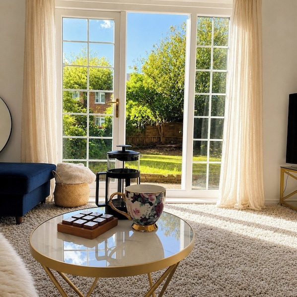 Ein Zimmer mit Glastisch, blauem Sofa, dekorativer Schale und Blick durch große Glasschwingtüren.