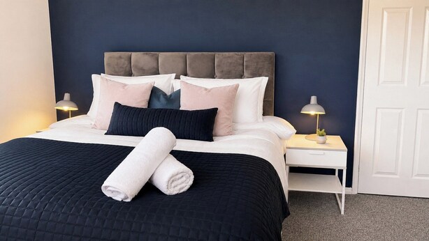A neatly made bed with a dark quilt, a headboard, and multiple pillows. - Modern 3BR | Close to Durham Centre (Belmont)