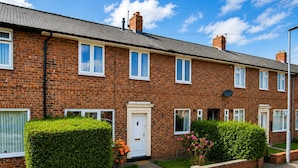 A row of brick terraced houses with white doors and windows, a clear sky, and well-maintained hedges. - Modern 3BR | Close to Durham Centre (Belmont)