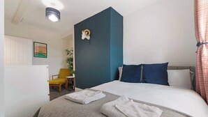Ein Hotelzimmer mit Bett, zwei Kissen, Kopfteil, Nachttisch, Sessel, Pflanze und Wanddeko.