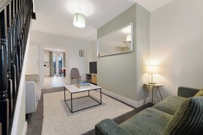 A modern living room with a sofa, a coffee table, a TV, and a lamp. - Modern and Fancy 2BR Durham | Contractor Rates (Sherburn Hill)