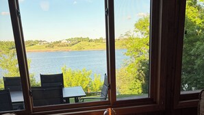 Ein Zimmer mit Tisch, Stühlen, einer Stehlampe und Blick auf einen See.
