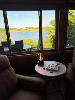 A room with a table, chairs, a table lamp, and a view of a lake.