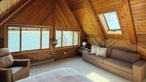 Ein gemütliches Schlafzimmer im Dachgeschoss mit einem großen Bett, einer Couch, einem Sessel und einem Deckenventilator.