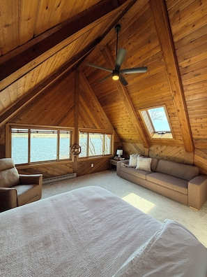 Ein gemütliches Schlafzimmer im Dachgeschoss mit einem großen Bett, einer Couch, einem Sessel und einem Deckenventilator.