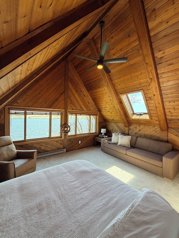 A cozy attic bedroom with a large bed, a sofa, a chair, and a ceiling fan.