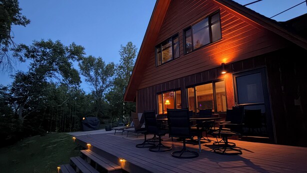 Ein modernes Haus mit einer Holzterrasse, Sitzgelegenheiten im Freien und einem großen Fenster mit Blick auf den Garten.
