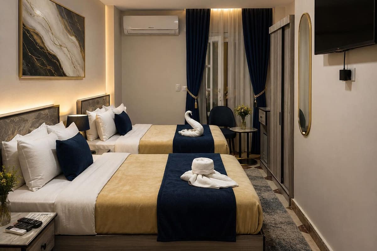 A hotel room with two beds, a TV, a flat-screen TV, a mirror, an air conditioning unit, and a vase with flowers.