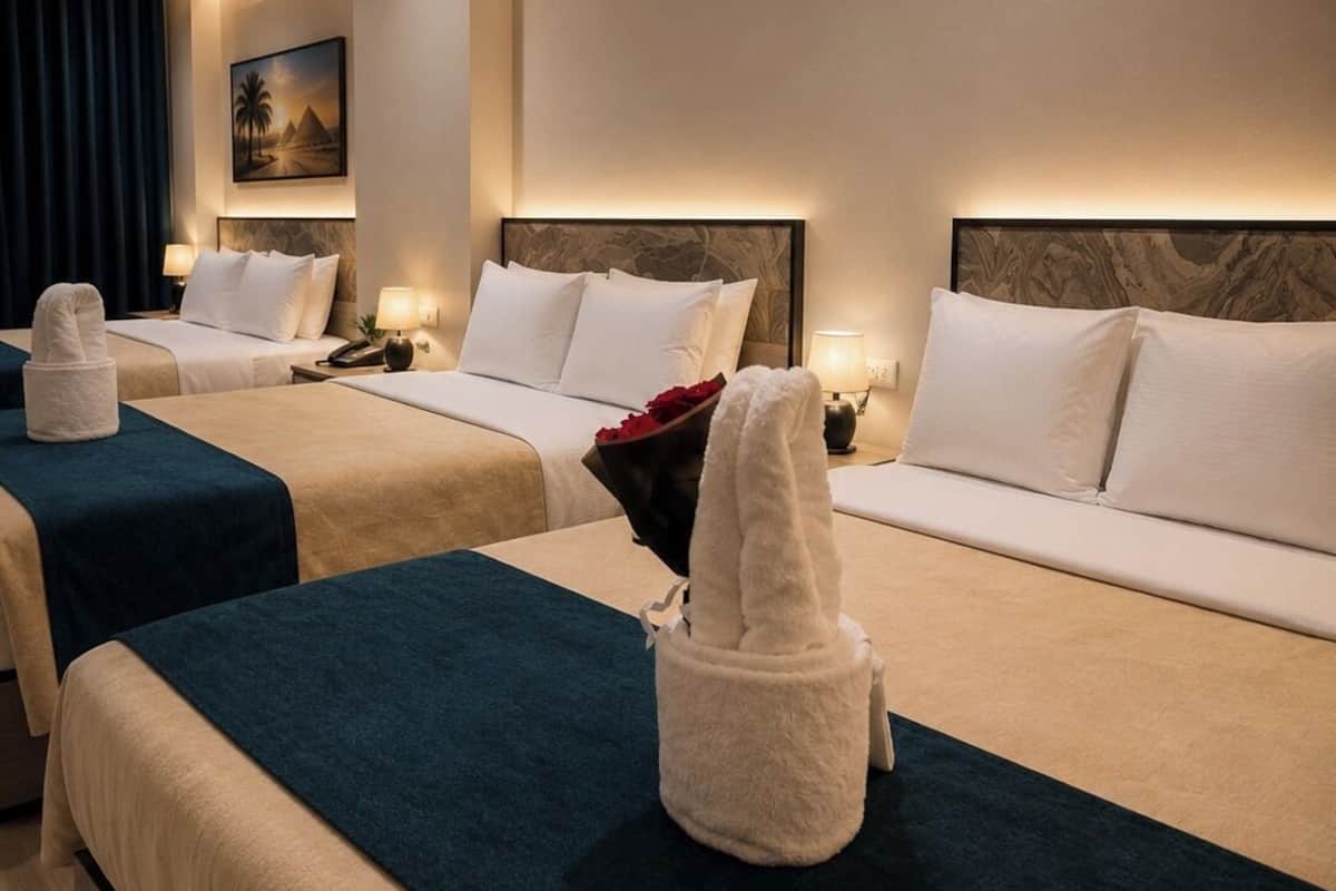 A hotel room with two beds, each with a headboard, bedside tables, lamps, and towels.
