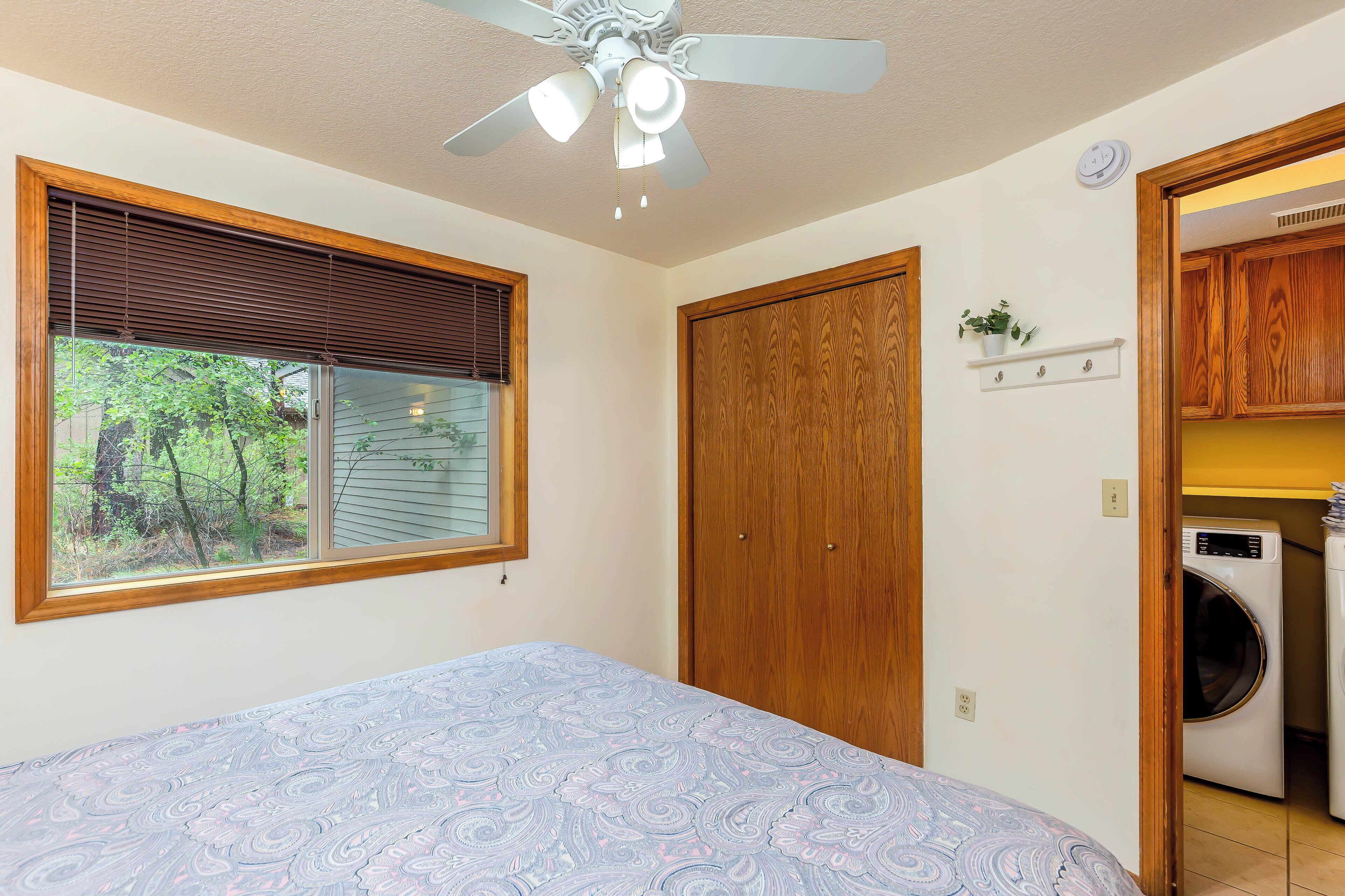 A bedroom with a bed, a ceiling fan, a window with blinds, a wooden door, and a laundry area with a washing machine.
