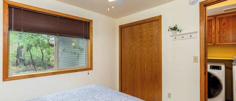 A bedroom with a bed, a ceiling fan, a window with blinds, a wooden door, and a laundry area with a washing machine.