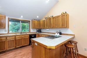 A kitchen with wooden cabinets, a large window, a built-in stove, and a bar stool. - NEW! 4BR | Hot Tub | Dogs | Sleeps 10 - CYPR16 (Sunriver)