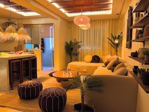 Ein modernes Wohnzimmer mit Sofa, Poufs, einem Couchtisch und einer Küchenzeile mit Bar.