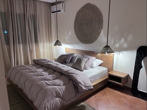 Ein Schlafzimmer mit Bett, Kopfstütze, Nachttischen, einer Wand-Klimaanlage und Wandverkleidung mit Struktur.