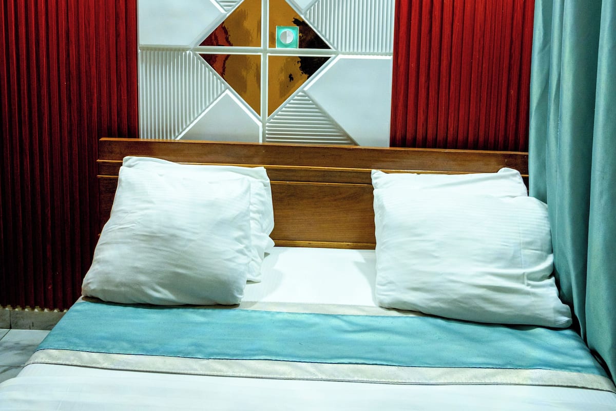 Una habitación de hotel con cama, cortinas rojas, diseño geométrico en la pared y cabecera de madera.