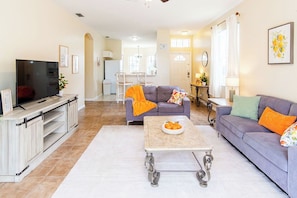 A living room with a television, sofas, a coffee table, and a kitchen area in the background.