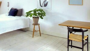 Ein Schlafzimmer im Loft-Stil mit freiliegenden Holzbalken, einem Bett, einem Tisch, einem Stuhl, einer hängenden Papierlaterne und zwei gerahmten Kunstwerken.