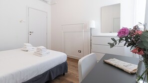 A hotel room with a bed, a table with a newspaper, a vase with flowers, and a mirror. - Italianway Easy - Ciardi 22 (San Siro)