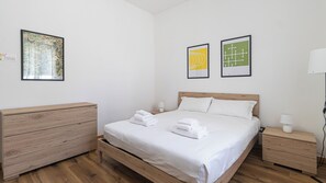 A hotel room with a wooden bed, white linens, a wooden dresser, two bedside tables, and two framed artworks on the wall. - Italianway Easy - Ciardi 22 (San Siro)