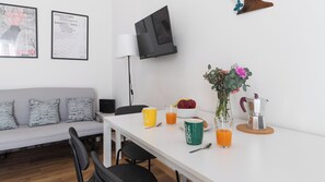 A modern living room with a white sofa, a dining table with breakfast items, a coffee maker, and framed artwork on the wall. - Italianway Easy - Ciardi 22 (San Siro)