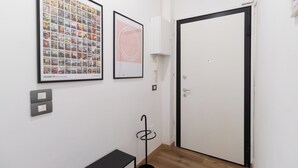 Een gang met een fotocollage in een lijst, een witte deur, een kapstok en een verdeeldoos.