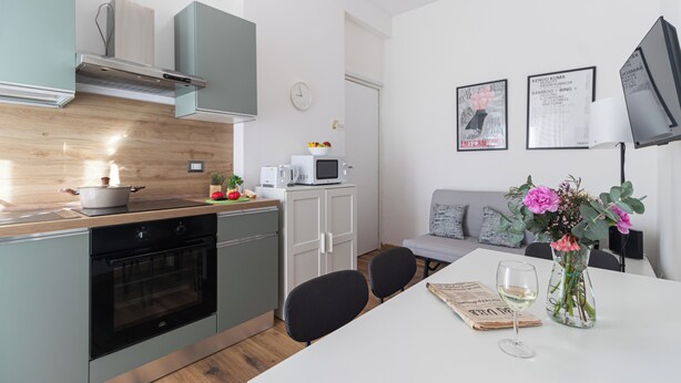 Een moderne keuken met een fornuis, oven, magnetron en kastjes. Er is een eethoek met een tafel, stoelen en een vaas met bloemen.