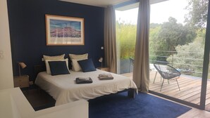Een slaapkamer met een bed, nachtkastje, stoel, raam en balkon.