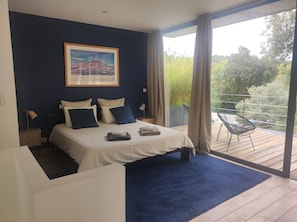 A bedroom with a bed, a nightstand, a chair, a window, and a balcony. - Architect's house in a wooded location - 8 minutes from the beach - Seignosse (Seignosse)