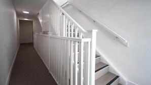 Ein schmaler, mit Teppich belegter Gang mit weißen Geländern und einer Treppe mit schwarzen Stufen.