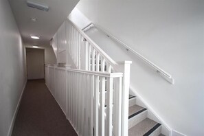 Ein schmaler, mit Teppich belegter Gang mit weißen Geländern und einer Treppe mit schwarzen Stufen.