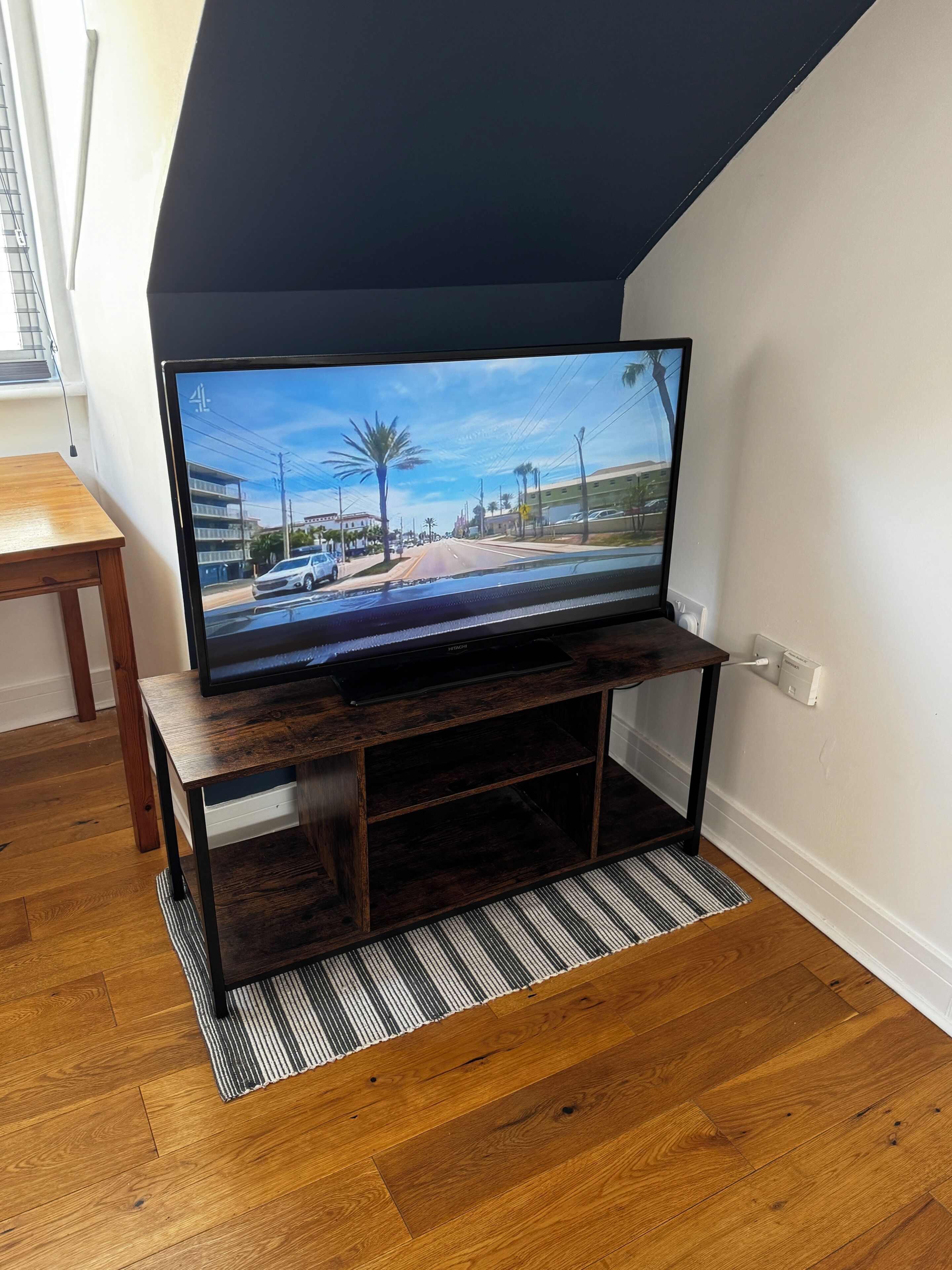 A flat-screen TV on a wooden stand in a room with wooden flooring and a striped rug.