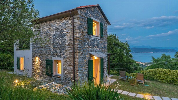 Una casa de piedra con contraventanas verdes, un camino de piedra y vistas al mar.