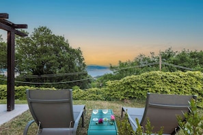 Zwei Gartenstühle mit Blick auf eine reizvolle Landschaft, dazwischen ein Tisch, eine Rose und ein Glas Wasser.