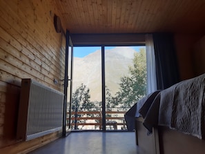 Habitación con interior de madera y un ventanal corredero que da a un espacio exterior con vistas a montañas.