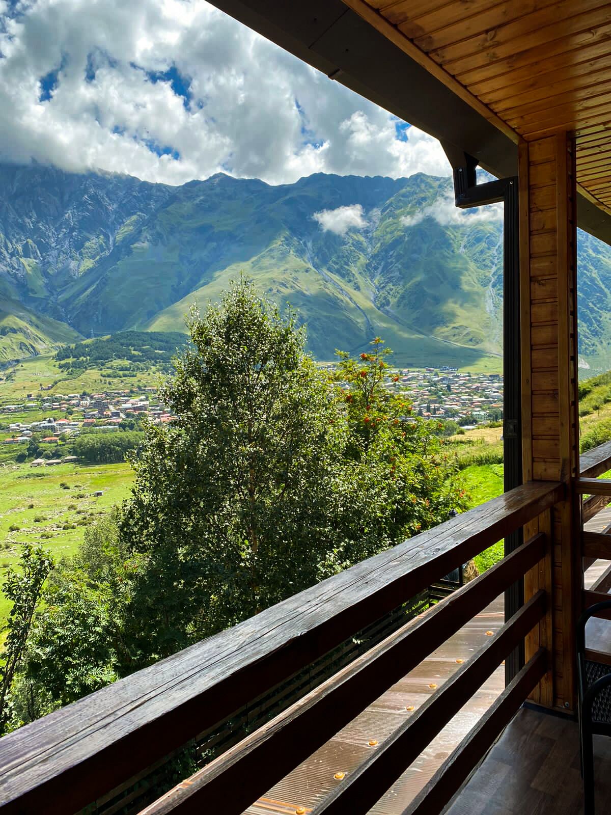 Un balcon en bois offrant une vue sur un paysage montagneux et sur une ville située en contrebas.