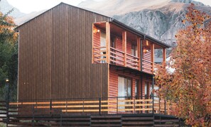 Una cabaña de madera con balcón, con montañas al fondo.